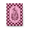 A hardcover notebook or journal with a pink and dark burgundy checkerboard cover, featuring a central illustration of a skeletal hand holding a crescent moon and stars, with roses at the bottom, shown on a white background.
