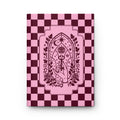 A hardcover notebook or journal standing upright on a white background. The cover features a pink and dark burgundy checkerboard pattern with a central pink arched illustration containing an eye, stars, crescent moon, roses, and a hand holding a wand.